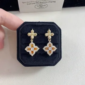 Detailed close-up of French retro gold earrings with orange quatrefoil stone design.