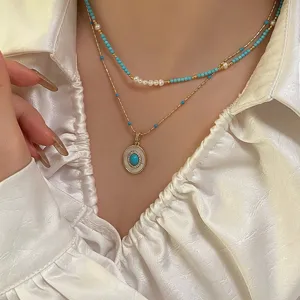 Close-up of layered necklace with freshwater pearls, turquoise beads and gold pendant.