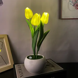 Luz nocturna LED de tulipán en maceta de cerámica sobre libro, detalle de decoración acogedora.