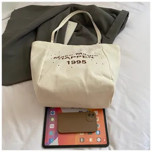 Große weiße Segeltuch-Tasche mit Make Magic-Druck, neben Telefon und Tablet gezeigt