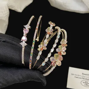 Vista dettagliata di bracciali dorati multistrato con fiori e cuori di cristallo colorato.