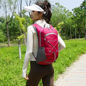 Red lightweight outdoor backpack for hiking and cycling worn by a model in a park.