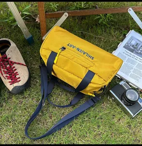 Detailansicht der gelben Outdoor-Umhängetasche mit Logo auf grüner Wiese