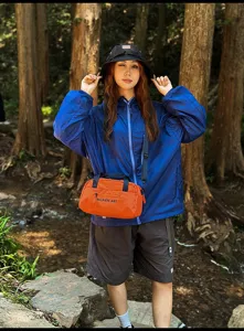 Model trägt eine leuchtend orangefarbene Sport-Umhängetasche in einem üppigen Wald im Freien