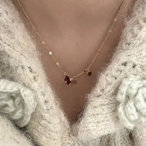 Close-up of gold-tone necklace with red enamel horse and heart charms on cream sweater. (91 chars)