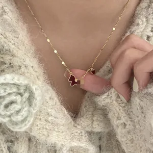 Close-up detail of vintage gold necklace with red horse and heart charms on sweater.