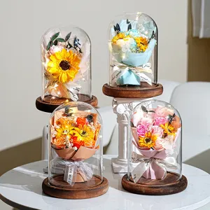Detailansicht von Sonnenblumen und Rosen in LED-beleuchteten Glaskuppeln auf Holzsockeln.