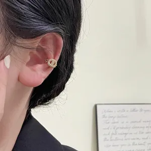 Macro view of a sparkling gold rhinestone CD logo ear cuff worn on a model's ear