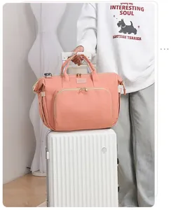 Elegante borsa per pannolini rosa con scomparti multipli su una valigia bianca
