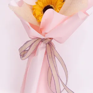 Detailed closeup of an artificial sunflower bouquet wrapped in pink paper with a rustic ribbon.