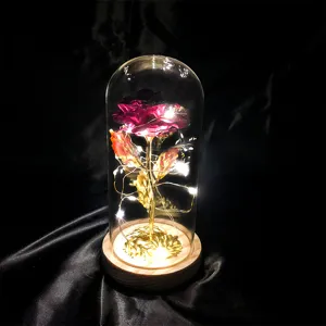 Detailansicht einer leuchtenden Goldfolienrose in einer Glaskuppel auf schwarzem Satinstoff.