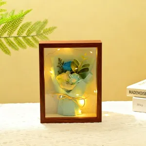 Marco de fotos de madera con ramo de flores artificiales azules y luces LED cálidas para decoración.