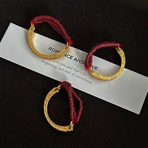 Close-up detail of C-shaped metallic texture rings with burgundy seed beads.