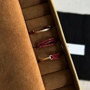 Detail of textured gold C-shaped rings and red seed bead elastic rings in a brown box.