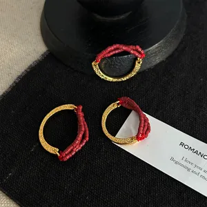 Close-up detail of C-shaped rings featuring metallic texture and red seed bead elastic bands