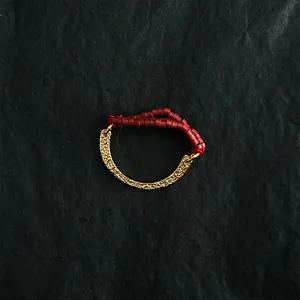 Macro detail view of elastic ring featuring hammered gold C-shape and red seed beads