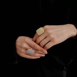 Primer plano de dos anillos con textura de malla cuadrada minimalista en las manos del modelo.