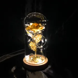 Verzauberte Goldfolien-Rose in Glaskuppel mit warmen LED-Lichterketten auf einem Holzsockel