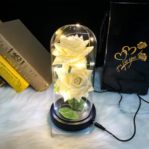 Primer plano de dos rosas blancas artificiales en una cúpula de vidrio con luz