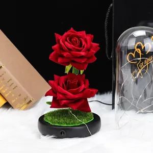 Primer plano de dos rosas de terciopelo rojo realistas con luces LED sobre una base negra