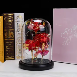 Primer plano de rosas rojas artificiales en cúpula de vidrio con luces LED y caja de regalo rosa