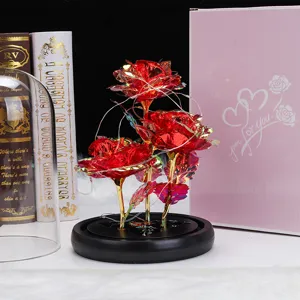 Detalle de tres rosas de lámina de oro iridiscentes con luces LED sobre base negra.