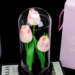 Gros plan d'une veilleuse doree sous cloche en verre avec tulipes roses et feuilles.