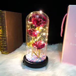 Detailed view of artificial gold foil roses inside a glass dome with glowing fairy LED lights.