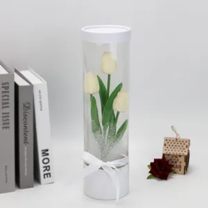 Detail view of the transparent PVC cylinder gift box featuring artificial white tulips inside.