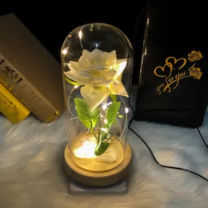 Vista detallada de una rosa blanca en cúpula de vidrio con luces LED sobre base de madera.