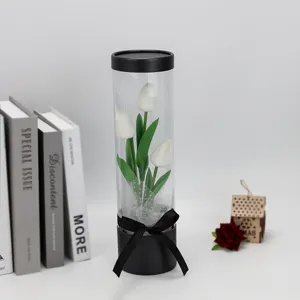 Detail view of artificial white tulips in clear PVC cylindrical box with black ribbon decor.