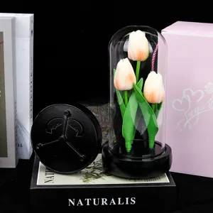 Détail de veilleuse tulipe sous dôme en verre avec fleurs artificielles et socle en bois noir.