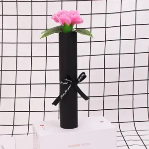 Pink soap carnation in a black tube box, resting on a white rectangular prop.