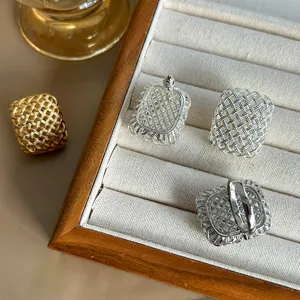 Vista detallada de pendientes y anillos con textura de rejilla en una bandeja de madera.