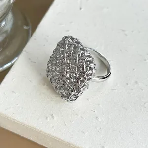 Primer plano de un anillo de plata con textura de malla y diseño tejido de rombo.