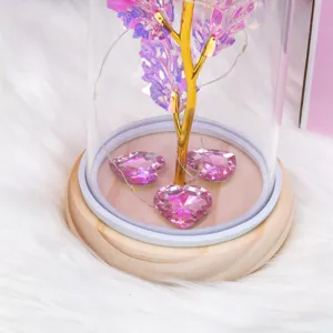 Detalle en primer plano de rosa luminosa bajo cúpula de cristal con corazones y base de madera.
