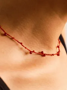 Detail view of a dainty hand-woven red cord necklace featuring small red agate beads