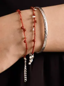 Close-up view of a hand-woven red string bracelet with agate beads and a silver bangle