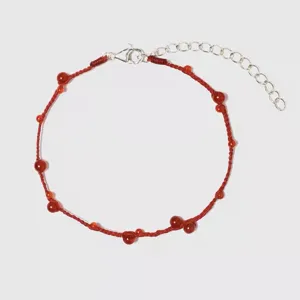 Detail showing a hand-woven red string bracelet featuring round carnelian beads.