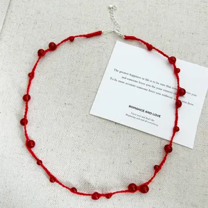 Handmade red string necklace with red agate beads on a minimalist white background card