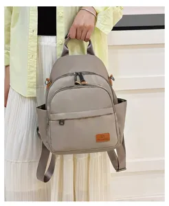 Grey canvas backpack detail showing front zipper pocket and brand logo patch design.