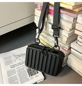 Vista detallada de un bolso bandolera rígido negro de tendencia con textura de maleta