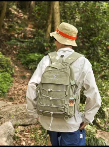Back view of a minimalist olive green large capacity backpack in an outdoor forest setting.