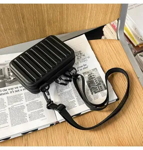 Detalle de un pequeño bolso rígido negro tipo maleta sobre un diseño de revista