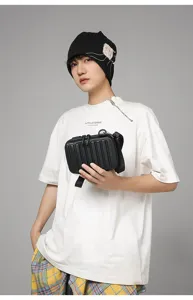 Modelo asiático luciendo un bolso bandolera rígido negro estilo maleta mini