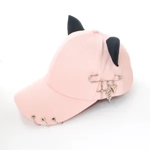 Close-up of pink baseball cap featuring black cat ears, metal rings and safety pin charms.