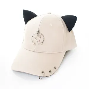 Vue détaillée d'une casquette beige avec oreilles de chat noires et anneaux métalliques.