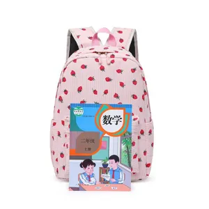 Pink strawberry print corduroy backpack shown with textbook for scale