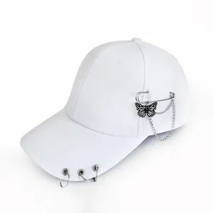 Close-up detail of a white baseball cap featuring metal rings on the brim and a butterfly chain pin.