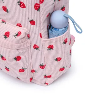 Detail of pink corduroy strawberry backpack side pocket holding a light blue umbrella.